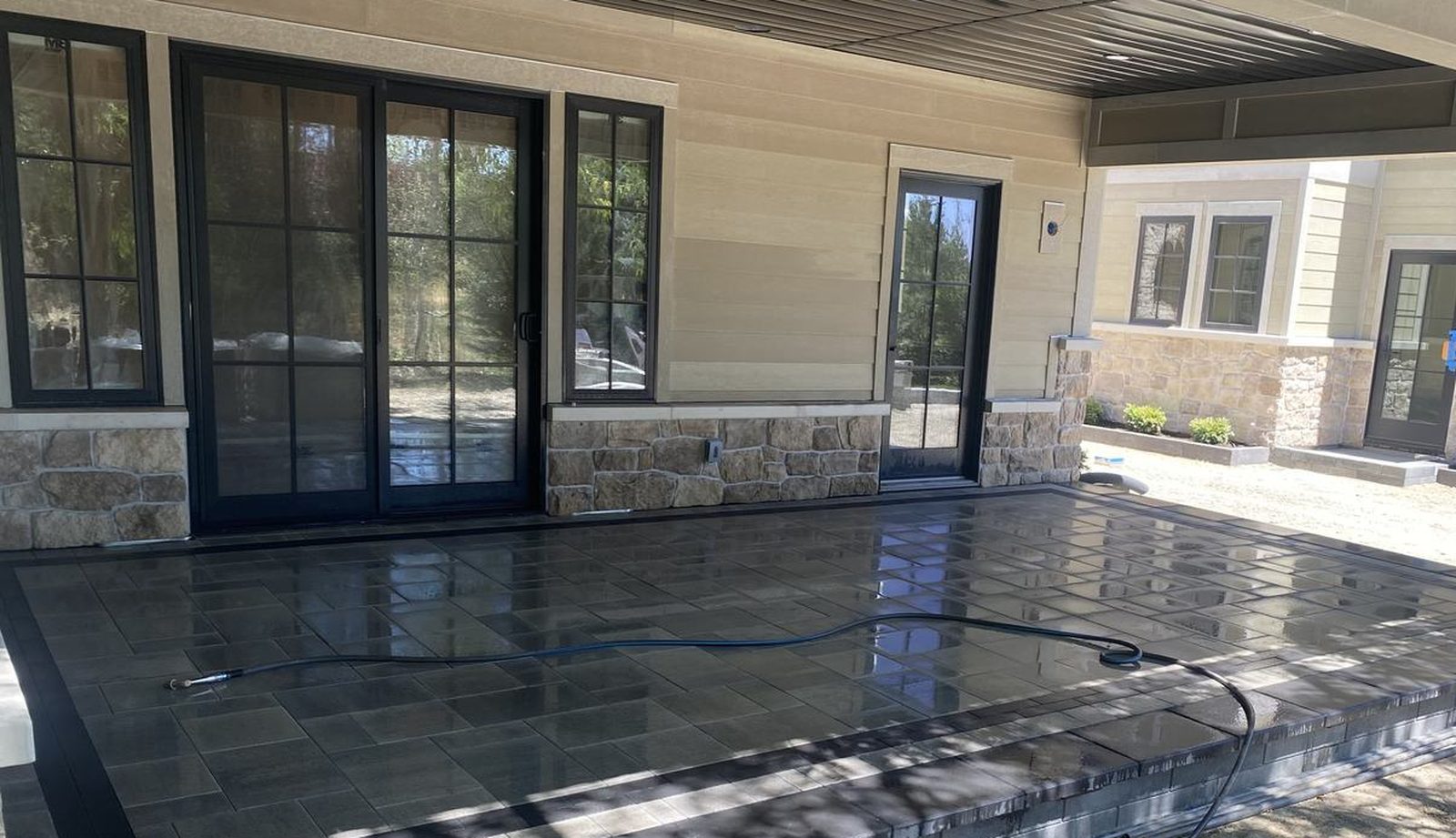 A covered patio with dark stone paving and full-height glass, opening onto the garden.