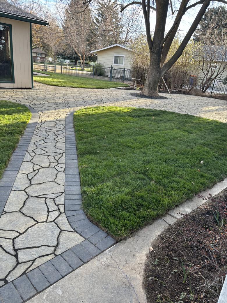 A flagstone path with a dark border, curving across a mown lawn.