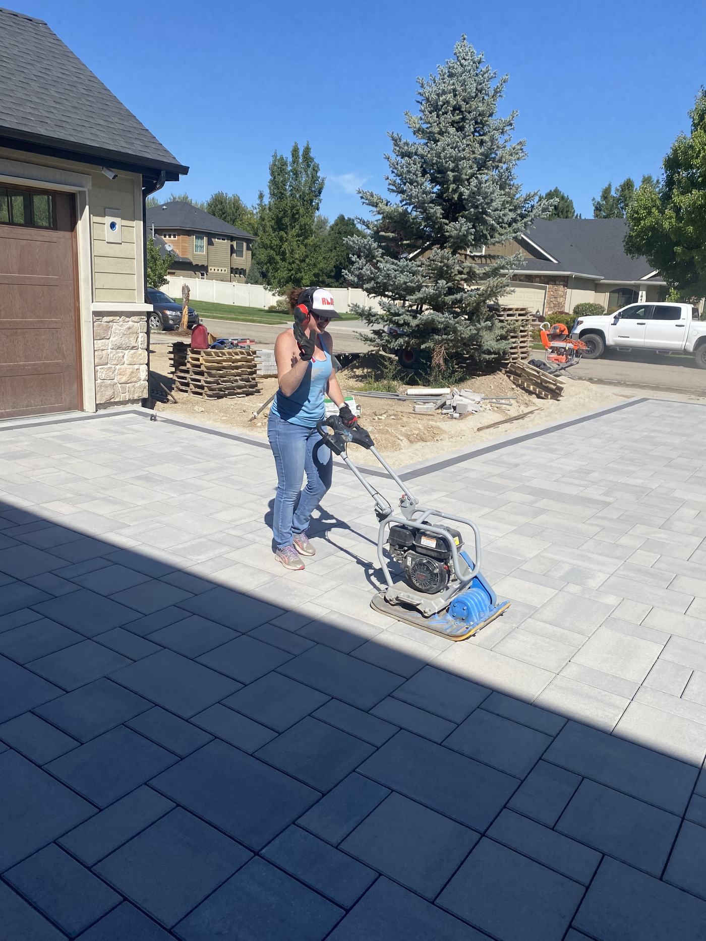 A crew member running a plate compactor across a newly laid paver driveway on another property.