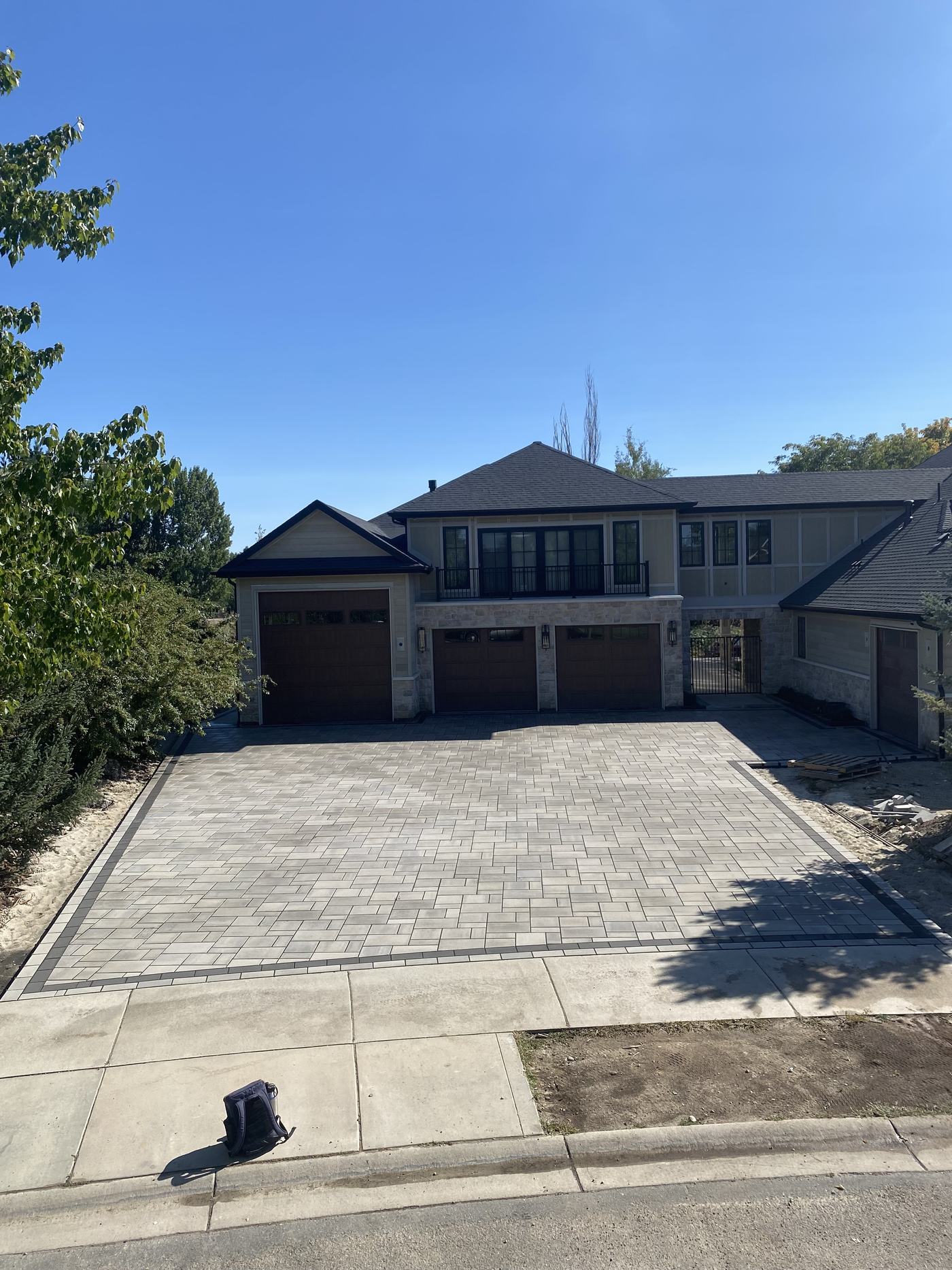 A finished interlocking paver driveway with a contrasting soldier-course border, sweeping up to a three-bay garage.