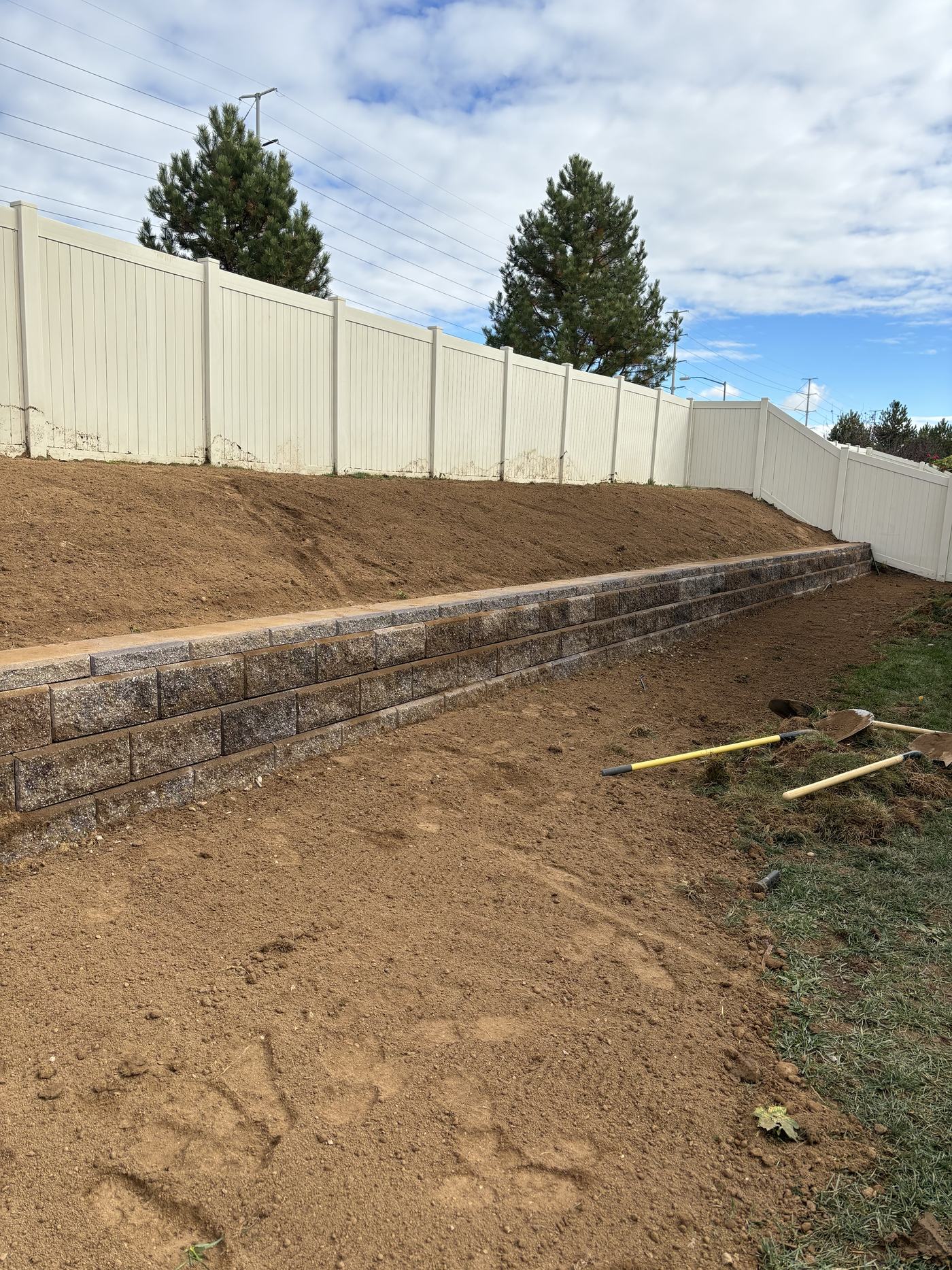 A newly built segmental block retaining wall with the slope behind it regraded back to bare soil.