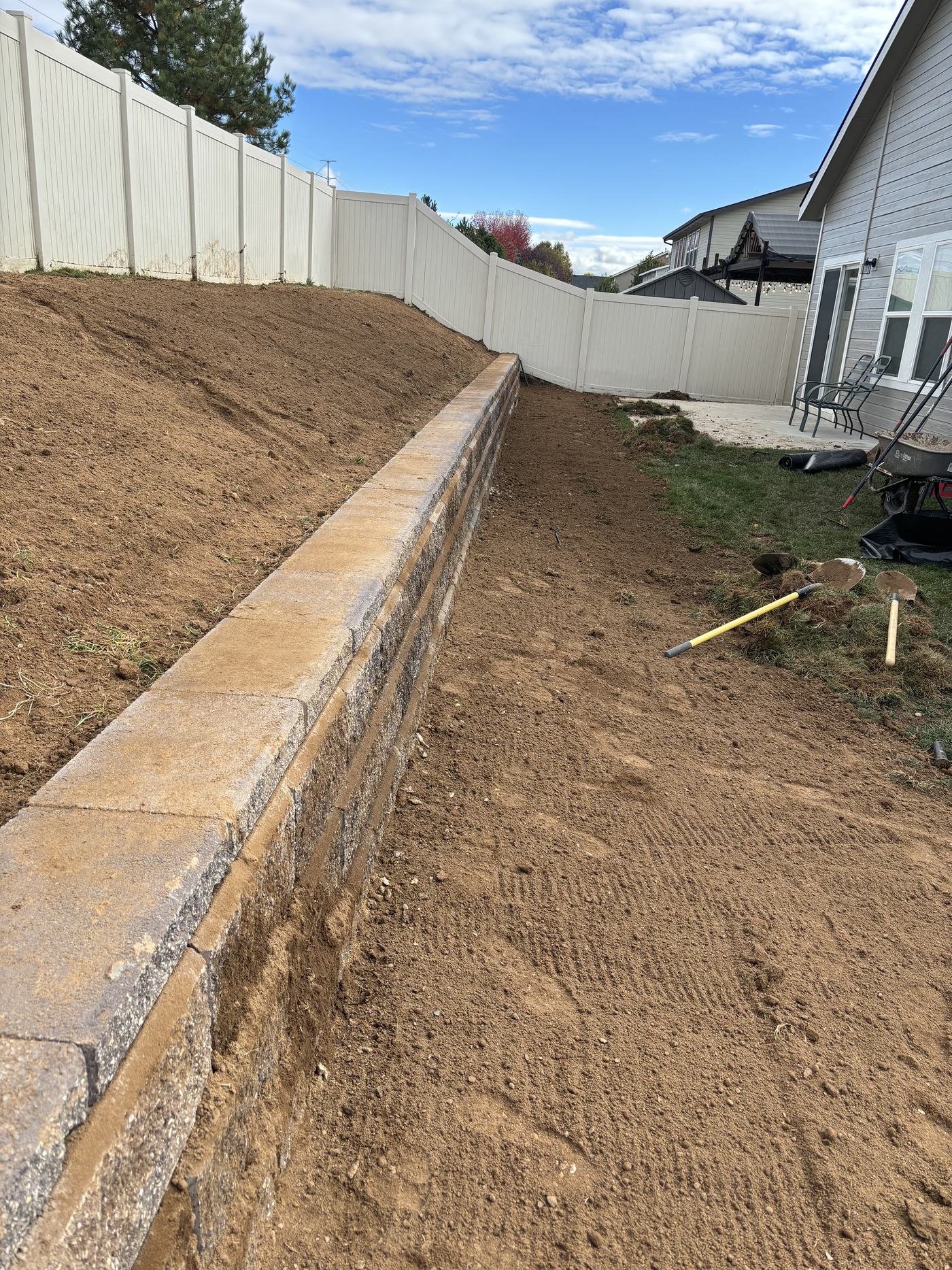 A long segmental block retaining wall holding a regraded slope, with freshly worked soil above it.